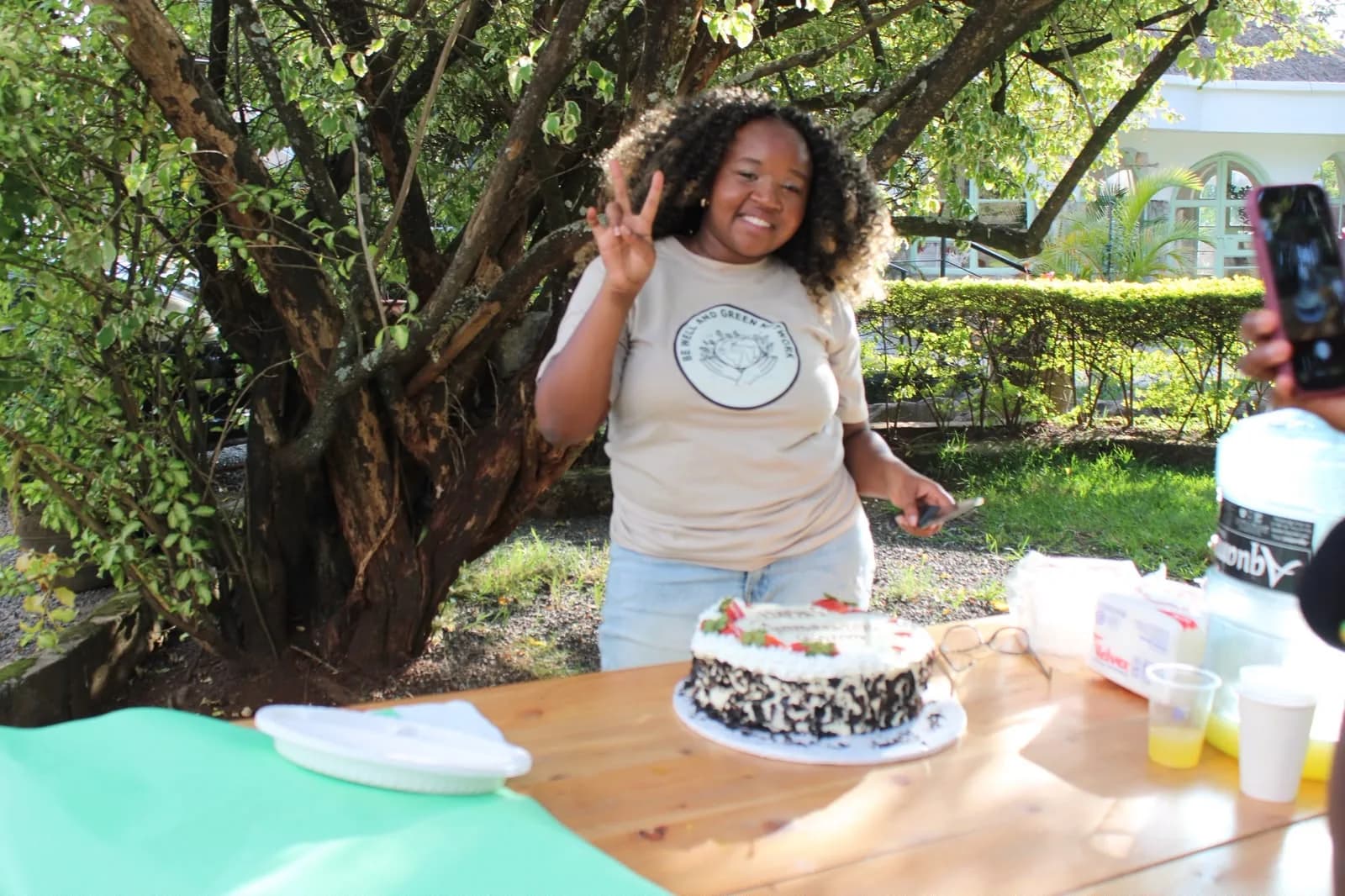 A BWGN volunteer in a branded T-shirt celebrating with a cake outdoors